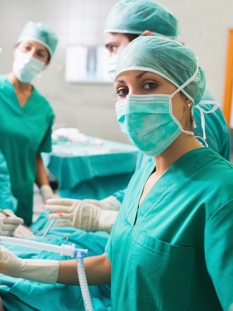 Nurse holding an oxygen mask on a patient while looking at camera in an operating theatre